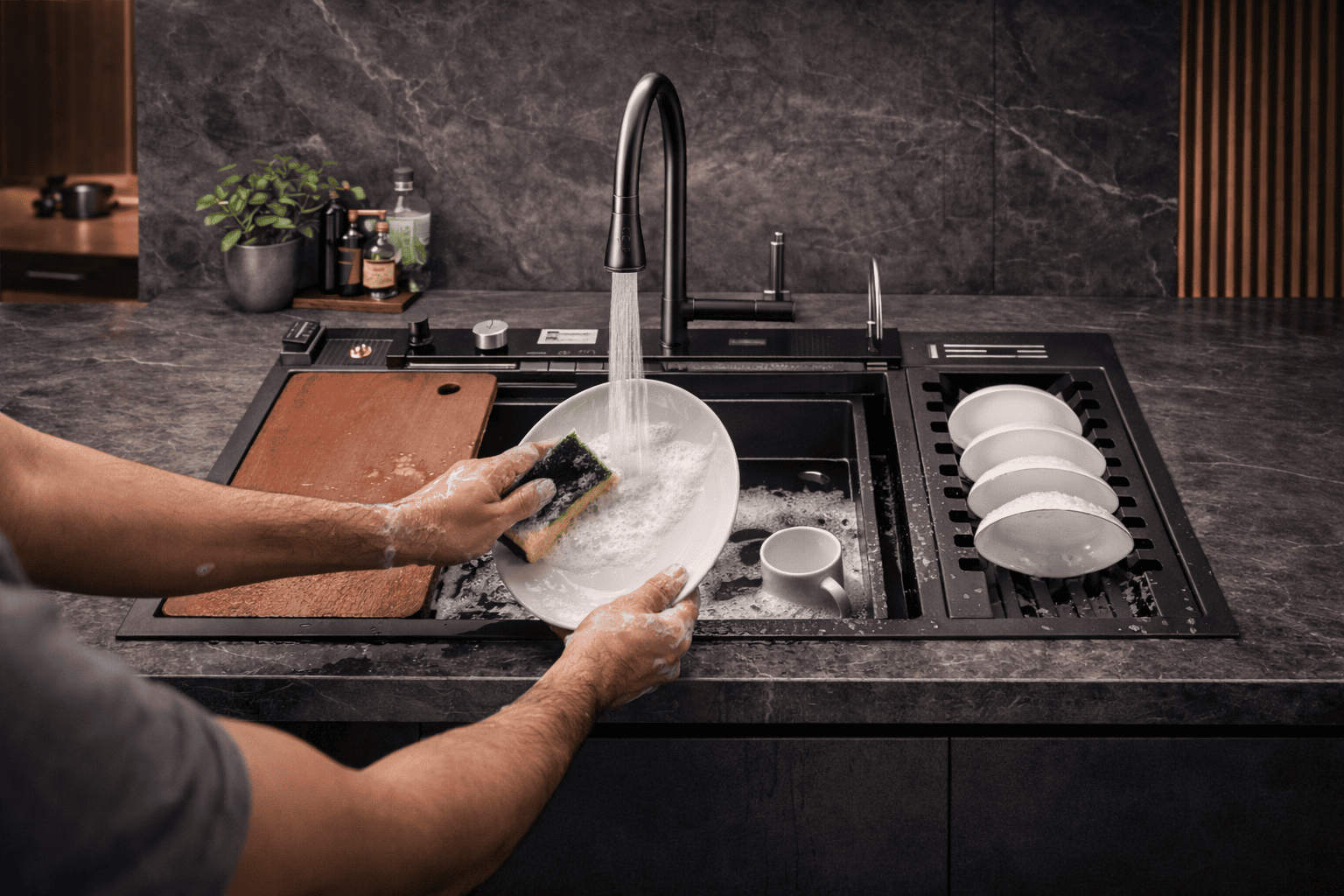 Person washing dishes in a modern kitchen sink with a dark countertop.