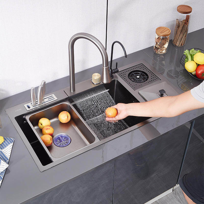 Person washing an orange in a modern kitchen sink with fruits and vegetables on the counter.
