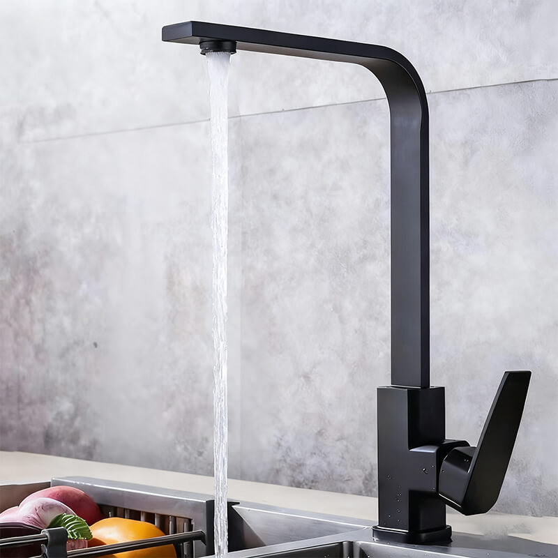 Black kitchen faucet with water flowing into a sink against a gray tiled wall.
